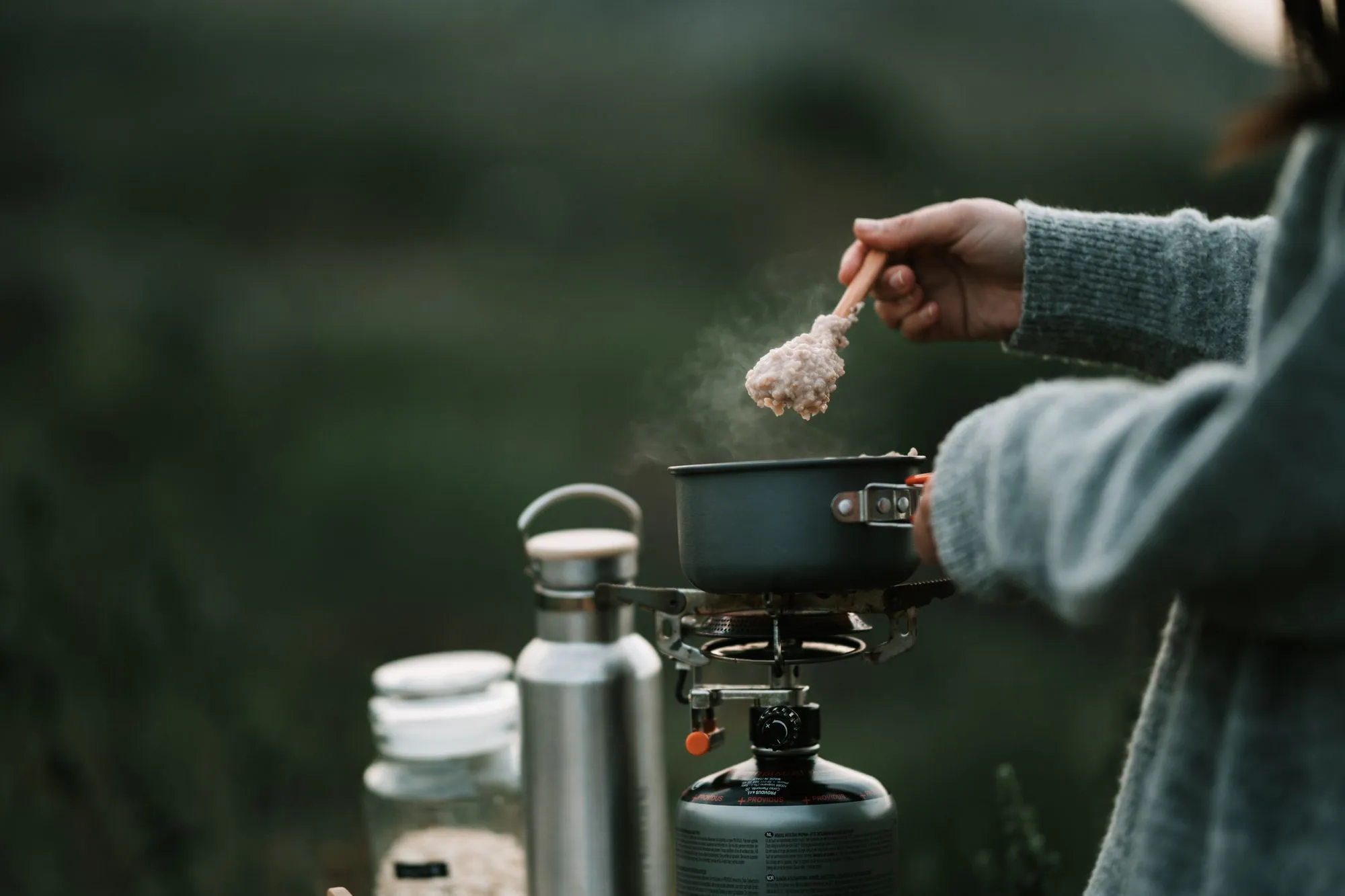Main qui assaisonne une casserole posée sur un réchaud de randonnée